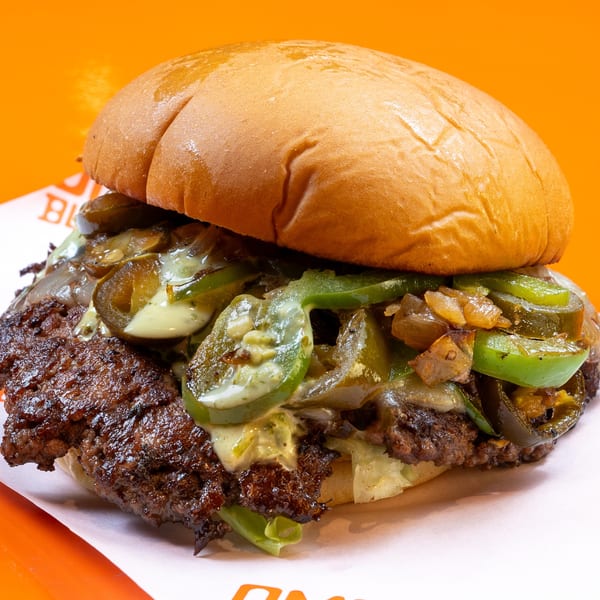 A close-up of a burger with a beef patty, melted cheese, grilled onions, and jalapeños.