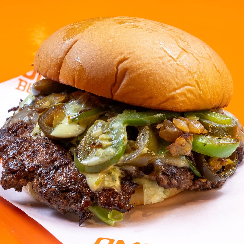 A close-up of a burger with a beef patty, melted cheese, grilled onions, and jalapeños.