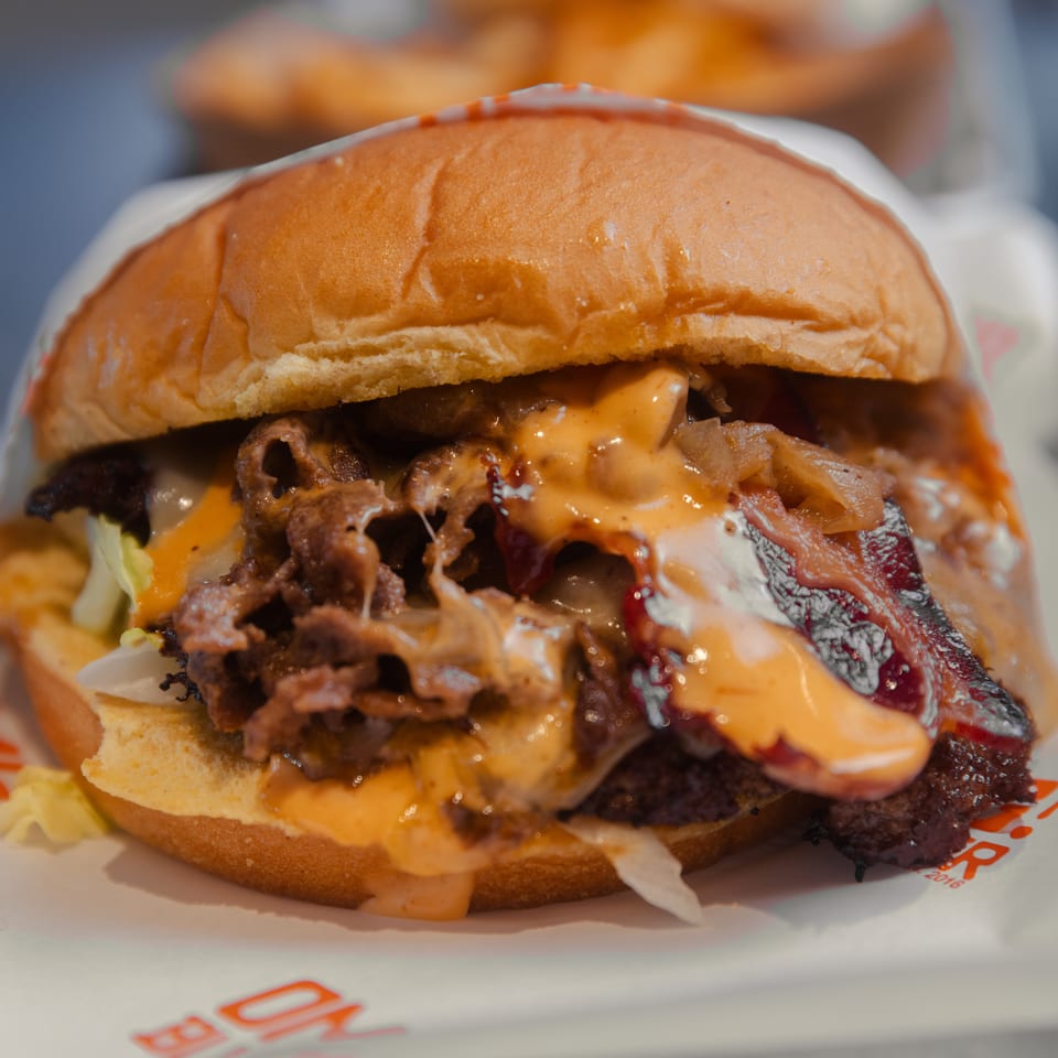 Close-up of a burger with melted cheese, bacon, caramelized onions, and lettuce on a bun.