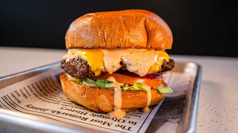Cheeseburger with melted cheese, special sauce, lettuce, tomato, and red onion on a brioche bun.