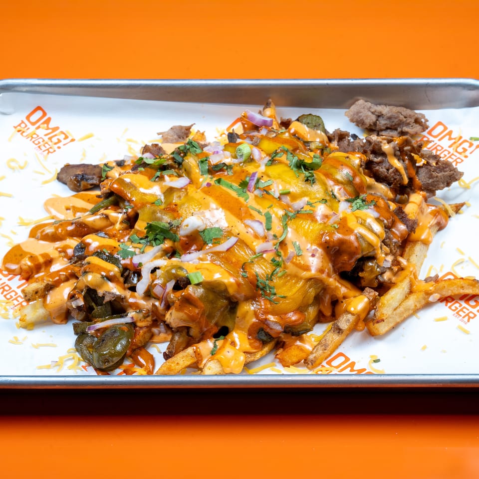 OMG! Burger loaded fries with cheese, meat, jalapeños, onions, and sauce on a metal tray.