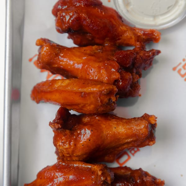 Six buffalo chicken wings with a side of ranch dressing on a metal tray with paper.